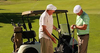 Two male friends chatting on the golf course by their kart