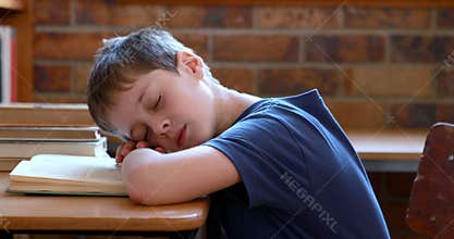 Little boy sleeping on a book in classroom