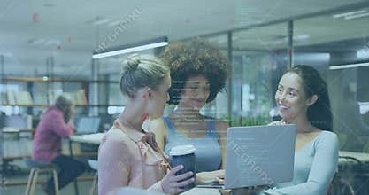 Collaborating three women wearing casual tops reviewing laptop code in open office, with coffee