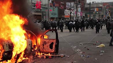 Riot police line walk towards crowd through fire