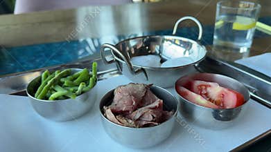 Tomatoes, beef, green beans, and poached eggs on a tray in iron pot-shaped dishes