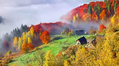 Colorful autumn landscape in the mountain village. Foggy morning