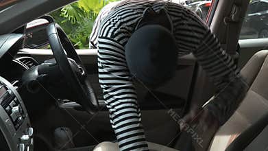 Masked thief in striped shirt reaching inside through open window stealing black briefcase and run away