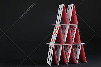 House of playing cards on black background, space for text