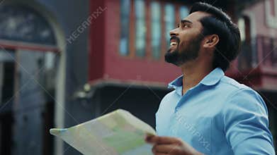 Portrait of amazed Indian male tourist with map looks around at landmark in city district