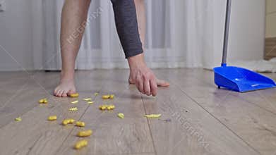 Person cleaning a mess of dropped snacks from a wooden floor with a dustpan
