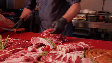 Chef hands throwing a chunk of raw lamb on the red table to chop it in pieces.