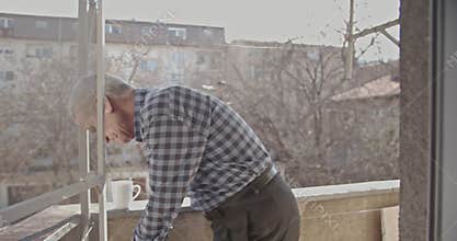 An Elderly Man Diligently Cleans His Balcony Railing on a Bright Sunny Day.