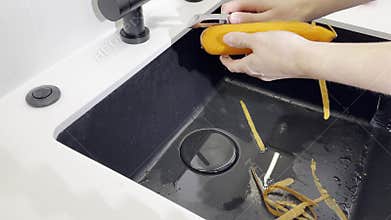 Peel vegetable ingredient. Hand holding peeler with blade over sink
