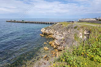 A calm day along a shoreline with undercut, eroded rocks and an ex-commercial jetty.