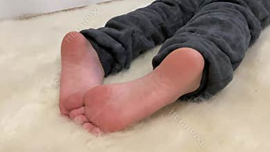 Close-up of barefoot child feet while boy lying on white fur and watching cartoons