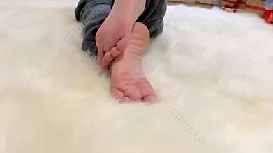 Close-up of barefoot child feet while boy lying on white fur and watching cartoons