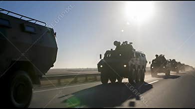 A Military Convoy Of Armored Vehicles Moves Along A Straight Highway Under The Bright Sun With Shimmering Heat Waves Visible