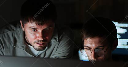 Two white Caucasian male software developers work late night on program coding in home office