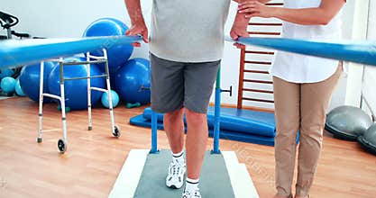 Physiotherapist helping patient walk with parallel bars