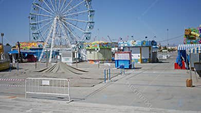 Fairground ferris wheel, closed stalls and empty walkways in soft defocused park; background backdrop copyspace overlay