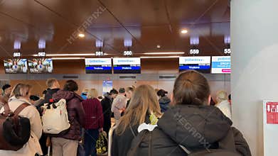 Queue of travelers waiting at airport check-in counter under digital flight displays