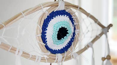 Handcrafted dream catcher shaped like a blue evil eye. Or nazar. Gently swinging. Combining spiritual protection amulets from