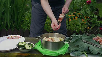Skewering marinated meat outside. Person prepares kebab over backyard grill