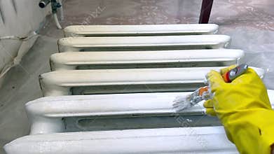 Hand in yellow glove painting radiator with white paint