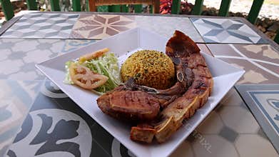Plate with grilled pork chop, tomato salad, and seasoned rice ball served on patterned table