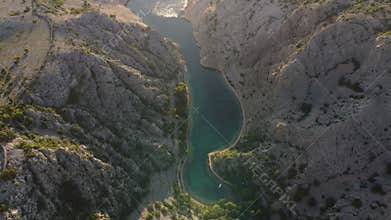Aerial view of a dramatic canyon with turquoise water surrounded by rugged rocky cliffs and sparse vegetation