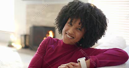 Reacting to fireplace crackle, woman reclining on sofa checking smartwatch then laughing at home