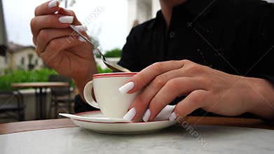Hands stirring coffee at outdoor cafe on a leisurely day