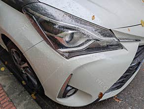 Car parked on a wet street in a quiet neighborhood during light rain with leaves scattered around