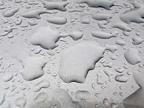 Water droplets collect on a smooth gray surface after a gentle rain in the early morning light near a city park
