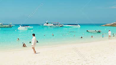 Tourists on the beach with white sand. Speedboats waiting at anchor