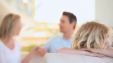 Sad child on a sofa while his parents are arguing