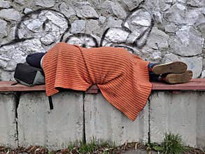 Down-and-out person with no fixed abode sleep on bench near grey stone wall