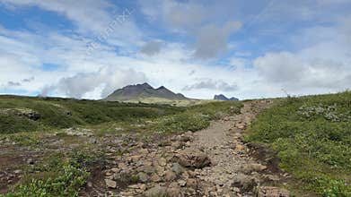 Gravel Trail Through Expansive Green Meadow with Distant Mountains in Iceland