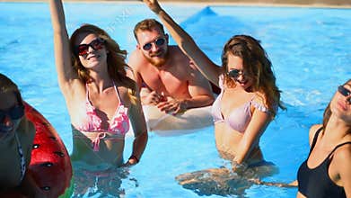 Friends have pool party dancing with inflatable mattress, watermelon floaty toys. Attractive hot pretty women in bikini