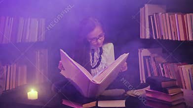 A girl opens a fairy-tale book in the library, colored smoke swirls around, candles are lit nearby