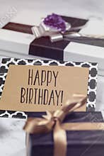 Happy Birthday card with gifts in black, white and gold colors.