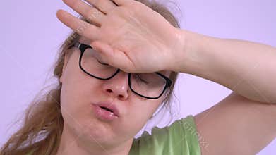Woman wearing glasses makes gesture of mopping her brow and fetching her breath