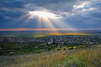 Scenic View Of A Village Light By Sun Through A Hole In The Clouds