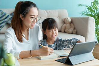Homeschooling. Asian family with daughter doing homework by using tablet with mother help. Asia mom and child learning online with