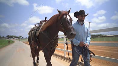 Tel Aviv, Israel - JULY 12, 2020: Brown stallion horse walking with his ranger cowboy man along a path at horse stables