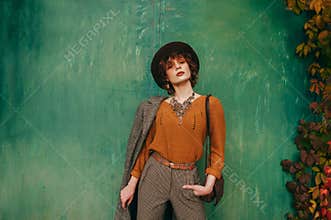 Fashion portrait of model in vintage clothing on green grunge wall background, looking into camera with serious face. Attractive