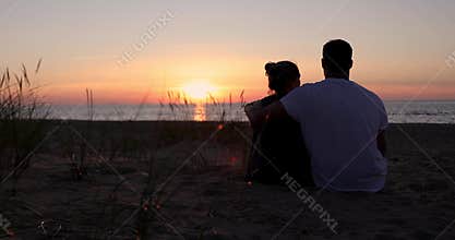 lovers couple sitting in sand on beach at romantic golden sunset. back view