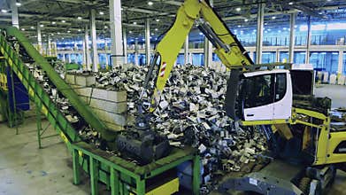Trash, e-waste, electronic garbage recycling factory. Backhoe tractor moves trash onto conveyor at a plant.