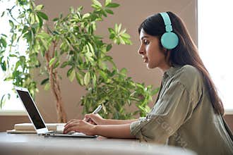 Indian teen girl student wear headphones watching online class making notes.