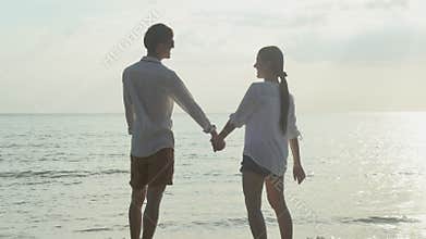 Happy asian couple walking with romantic and holding hand on the beach in summer for leisure together.