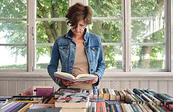 Middle aged woman reading a book in old bookshop