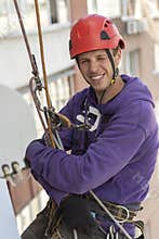 Industrial alpinism. Smiling worker hanging on ropes.