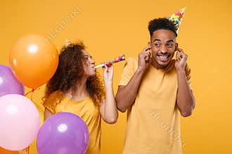 Funny friends couple african american guy girl in birthday hat isolated on yellow background. Holiday party concept
