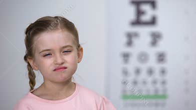 Little girl trying to read letters from eye chart, diagnostic of nearsightedness